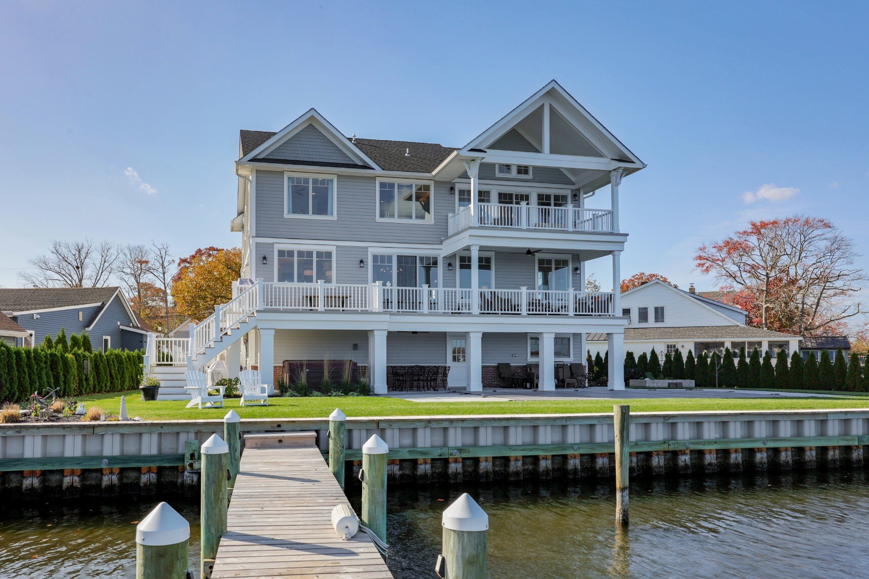 Back view of a spacious custom home by GTG Builders in Brick, NJ, featuring large balconies, a landscaped lawn, and a private dock