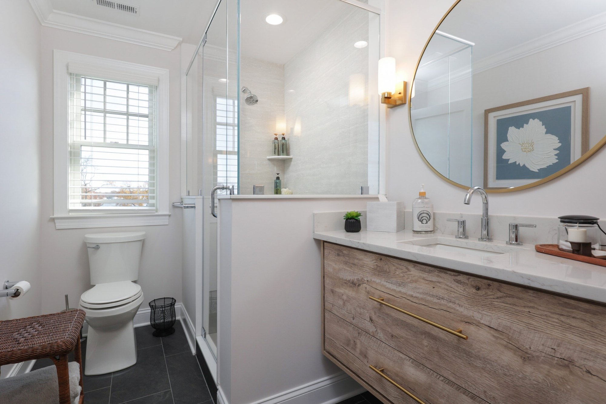 Modern bathroom with glass shower, rustic wood vanity, and round mirror in a custom home by GTG Builders in Brick, NJ.