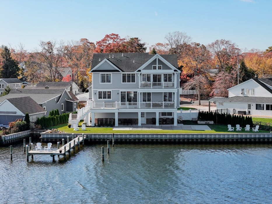 Straight-on view of a GTG Builders three-story waterfront home featuring balconies, a dock, and a landscaped backyard in Brick, NJ