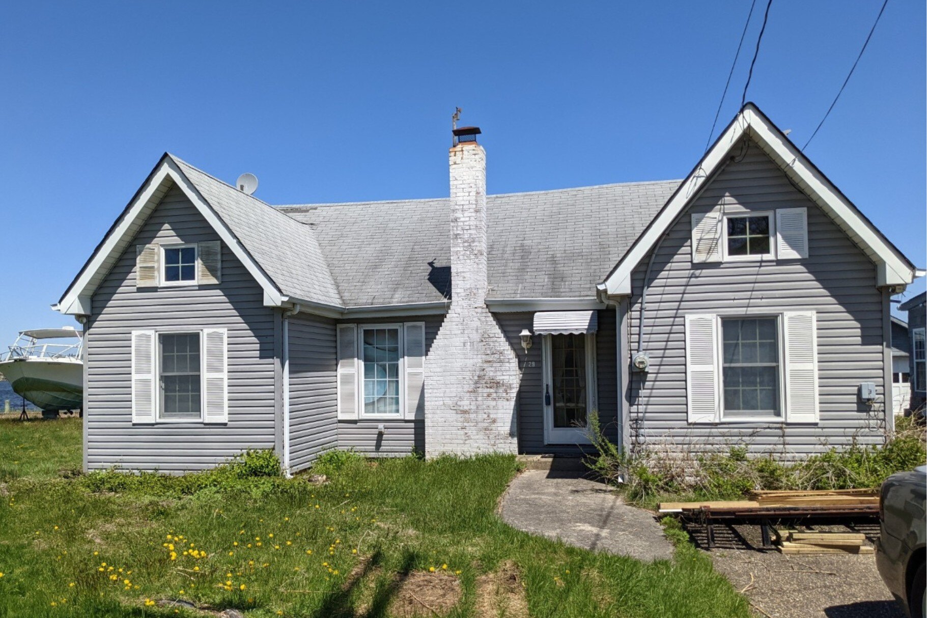 A modest waterfront cottage with a gray exterior and gable roof, awaiting renovation or rebuild on a scenic lot